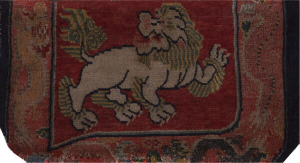 A textured, deep red rug features a central tan and green patterned mythological lion motif.