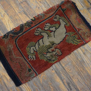 Small, low-pile red rug with a central khaki animal motif resting on distressed wood planks.