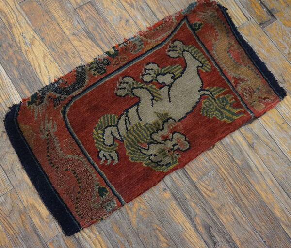 Small, low-pile red rug with a central khaki animal motif resting on distressed wood planks.
