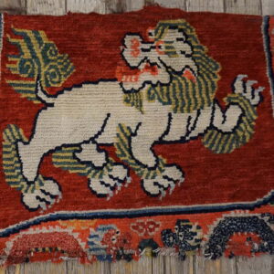 Worn, high-pile rug featuring a cream lion on a dark red field, resting on gray wood boards.