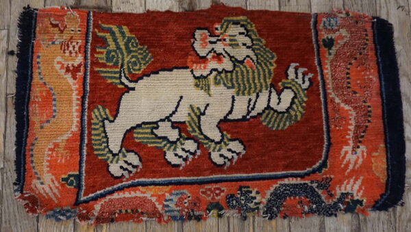 Worn, high-pile rug featuring a cream lion on a dark red field, resting on gray wood boards.