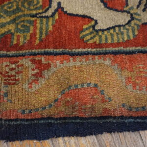 A thick-piled rug featuring complex red, gold, and blue patterns rests on wood flooring.