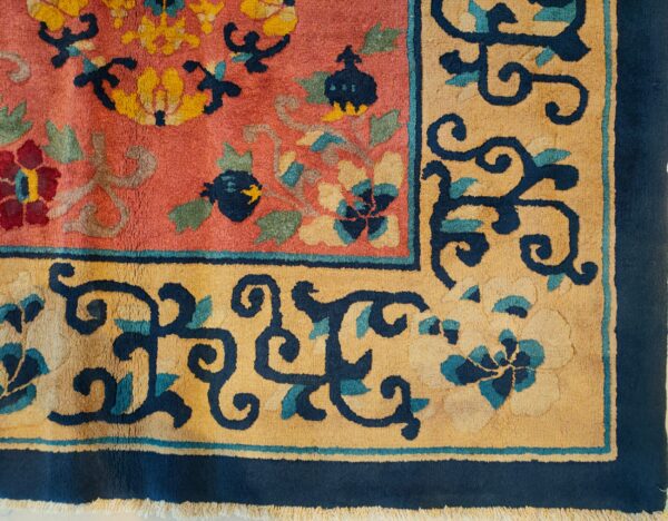 Close-up of a pink rug featuring an elaborate floral pattern in navy, gold, burgundy, and sage green.