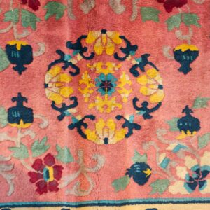 Close-up of a pink rug featuring an elaborate floral pattern in navy, gold, burgundy, and sage green.