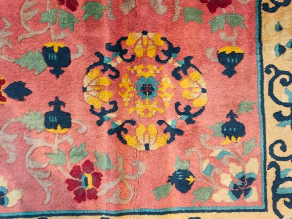 Close-up of a pink rug featuring an elaborate floral pattern in navy, gold, burgundy, and sage green.