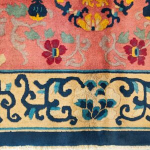 Close-up of a pink rug featuring an elaborate floral pattern in navy, gold, burgundy, and sage green.