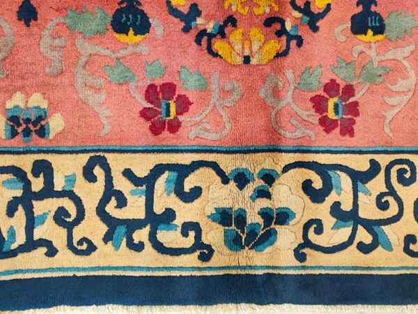Close-up of a pink rug featuring an elaborate floral pattern in navy, gold, burgundy, and sage green.