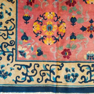 Close-up of a pink rug featuring an elaborate floral pattern in navy, gold, burgundy, and sage green.