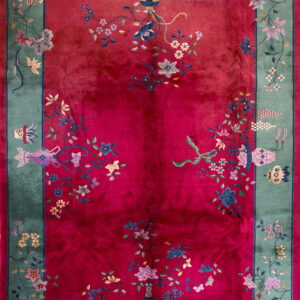 Deep red rug with a sage green border featuring intricate floral motifs and symbolic decorative objects.