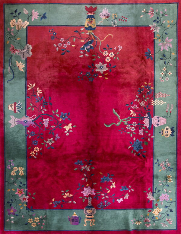 Deep red rug with a sage green border featuring intricate floral motifs and symbolic decorative objects.