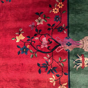 Deep red rug with a green border and multicolored yellow, blue, and pink floral patterns.