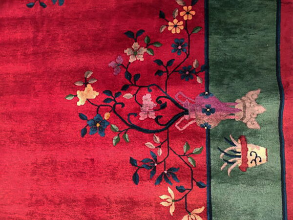 Deep red rug with a green border and multicolored yellow, blue, and pink floral patterns.