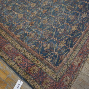 Muted blue and gold floral rug with a rust border, shown on weathered wood plank flooring.