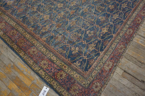 Muted blue and gold floral rug with a rust border, shown on weathered wood plank flooring.