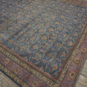 Blue rug with a gold and red faded floral trellis pattern rests on worn wooden planks.