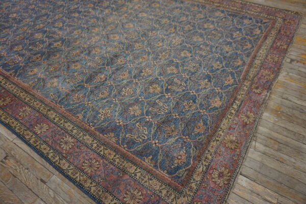 Blue rug with a gold and red faded floral trellis pattern rests on worn wooden planks.
