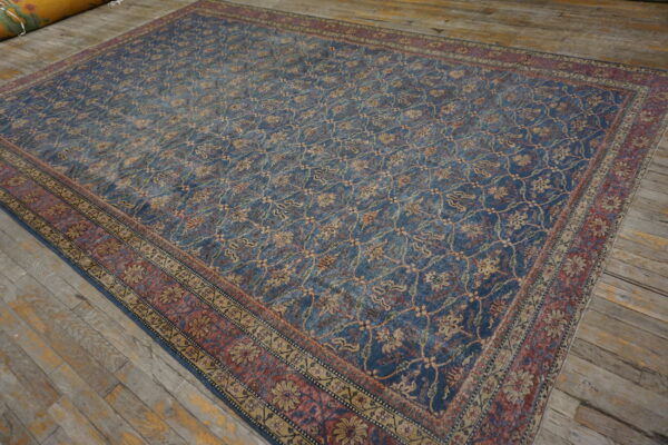 A large distressed blue rug with a beige vine pattern and red border lies on rustic wood floors.