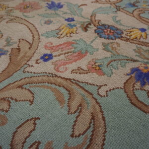 Close-up of a rug with scrolling floral and vine motifs in beige, mint, blue, brown, and pink.