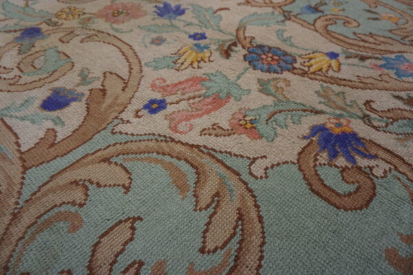 Close-up of a rug with scrolling floral and vine motifs in beige, mint, blue, brown, and pink.