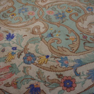 Ornate rug pattern with large brown scrolls, light teal ground, beige accents, and colorful flowers.