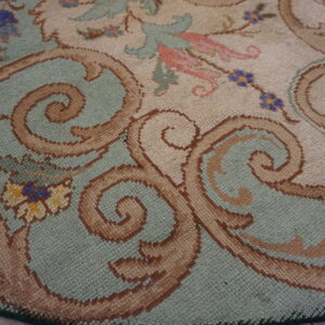 Close-up of a sage green and cream rug with large brown scrolling motifs and small floral accents.