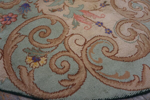 Close-up of a sage green and cream rug with large brown scrolling motifs and small floral accents.