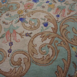 Traditional rug detail showing tan scrolls and colorful flowers against cream and light aqua backgrounds.