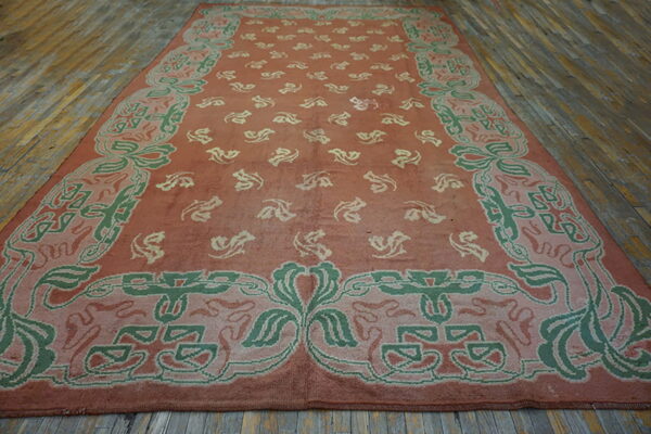Large pink and green patterned rug with a decorative border covering rustic wood flooring.
