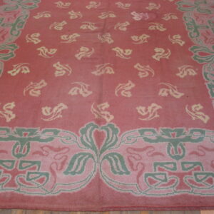 A rose and green rug with a stylized floral pattern and pale yellow motifs, lying on hardwood floors.