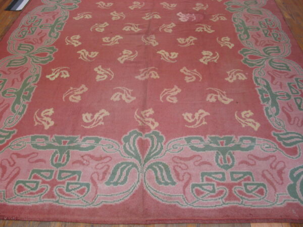 A rose and green rug with a stylized floral pattern and pale yellow motifs, lying on hardwood floors.