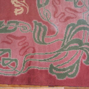 Low-pile rug detail showing stylized pink, green, and cream patterns on a red background over wood flooring.