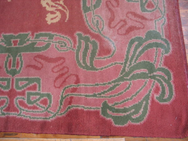 Low-pile rug detail showing stylized pink, green, and cream patterns on a red background over wood flooring.