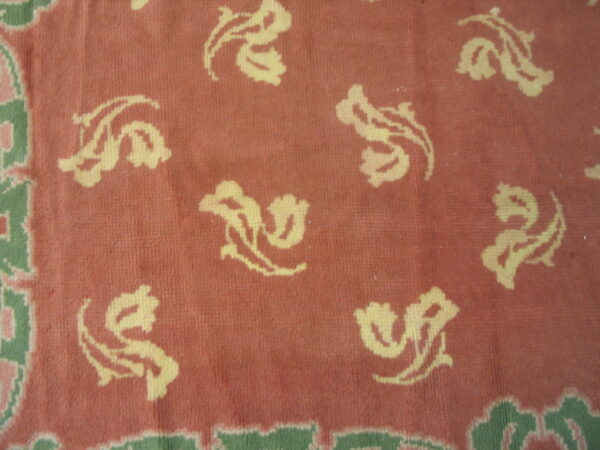 Close-up of a low pile coral rug patterned with pale yellow swirling floral motifs and a green border.