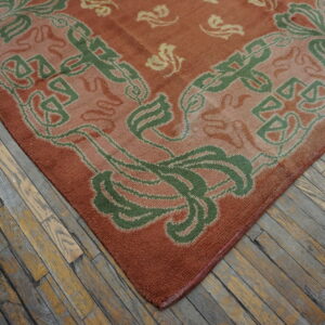 Rust-colored rug with green and beige stylized designs rests on distressed wood plank flooring.