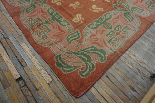 Rust-colored rug with green and beige stylized designs rests on distressed wood plank flooring.