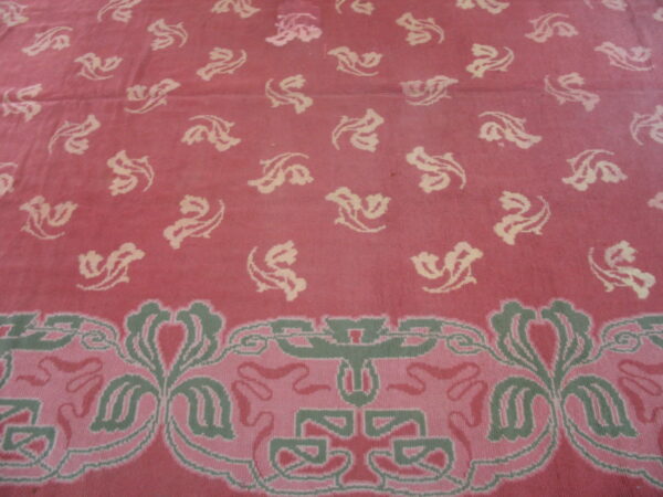 Rose pink rug with scattered cream floral motifs and a detailed border in sage green and lighter pink.