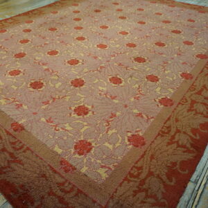 A low-pile floral rug in pink, red, and yellow colors is displayed on distressed wooden floorboards.