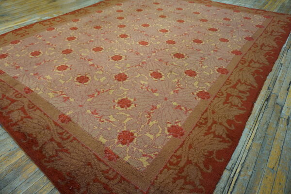 A low-pile floral rug in pink, red, and yellow colors is displayed on distressed wooden floorboards.