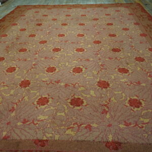 Repeating red and yellow floral patterns cover this large mauve rug displayed on wood flooring.