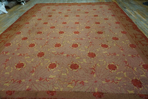 Repeating red and yellow floral patterns cover this large mauve rug displayed on wood flooring.