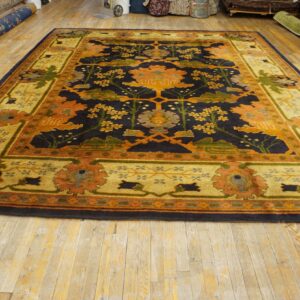 Ornate rug featuring a dark navy floral field and a wide gold-toned, multicolored border on wood floors.