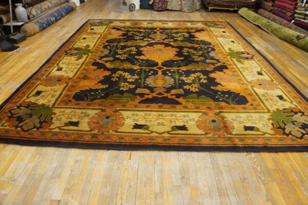 Ornate rug featuring a dark navy floral field and a wide gold-toned, multicolored border on wood floors.