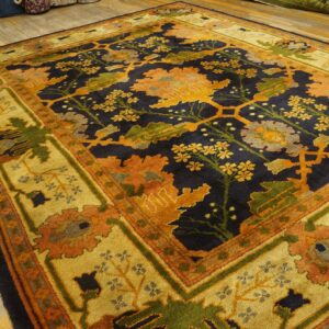 Large traditional rug with a navy floral field, wide gold border, rust, and green accents on wood floor.