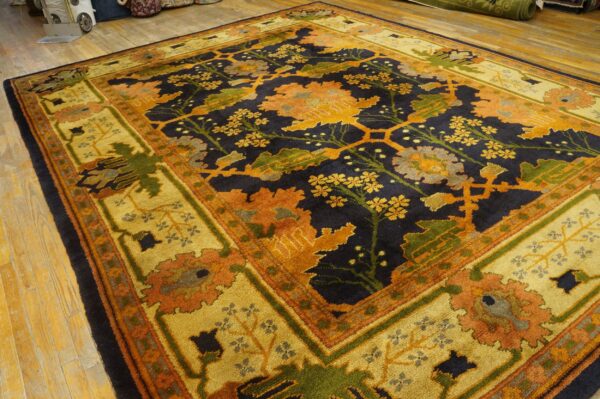 Large traditional rug with a navy floral field, wide gold border, rust, and green accents on wood floor.