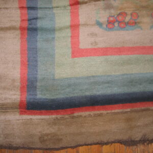Worn, plush rug border with wide stripes of brown, coral, blue, and sage rests on a wood floor.