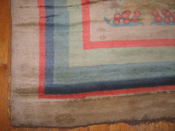 Worn, plush rug border with wide stripes of brown, coral, blue, and sage rests on a wood floor.