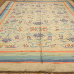 Cream floral rug with blue and coral motifs and striped borders rests on hardwood flooring.