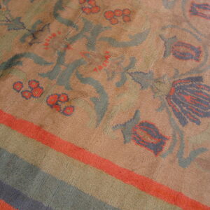 A close view of a rust-toned rug featuring stylized blue, green, and orange floral designs with striped edging.