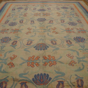 Beige rug with navy, light blue, and orange floral designs and a striped border on wood floors.