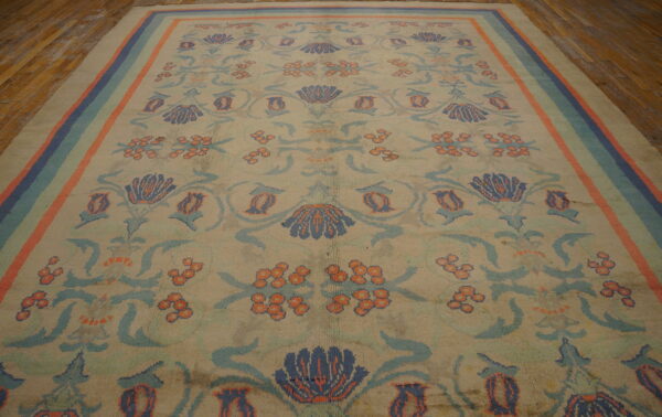 Beige rug with navy, light blue, and orange floral designs and a striped border on wood floors.